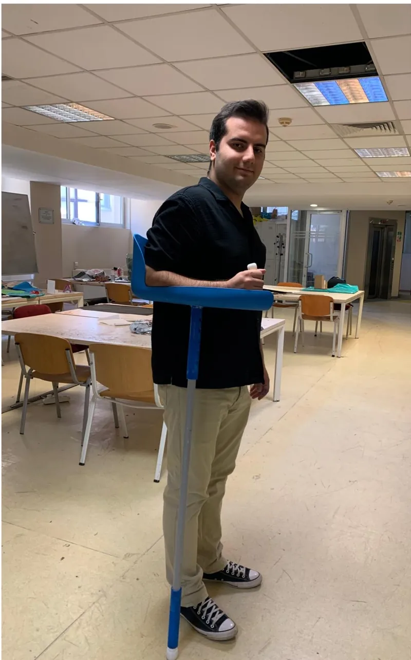 Atölyede prototip bastonu koluna takmış ayakta duran tasarımcı.